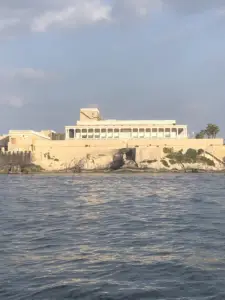 Historic limestone building with a columned facade atop Malta's fortified rocky coastline, seen from the water.