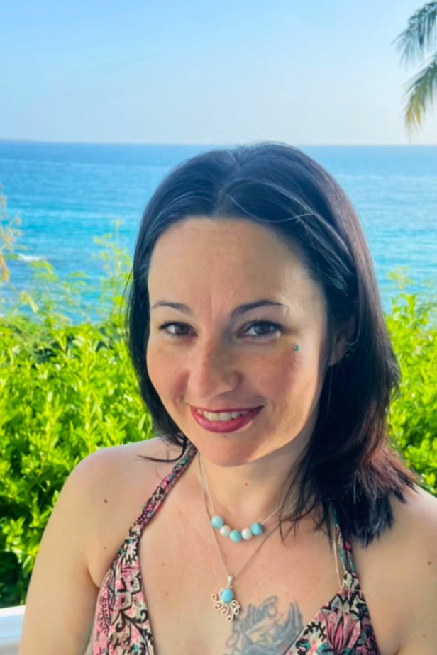 Jessica Gray, personal travel advisor and founder of Superbly Justifiable Travel Services, smiling in front of a tropical ocean backdrop