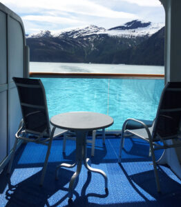 Private cruise ship balcony overlooking turquoise water and snow-covered mountains in Alaska