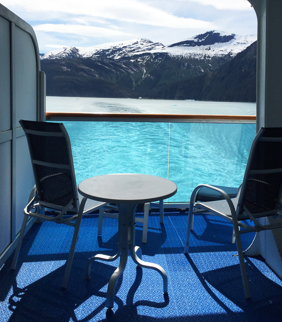 Private cruise ship balcony overlooking turquoise water and snow-covered mountains in Alaska