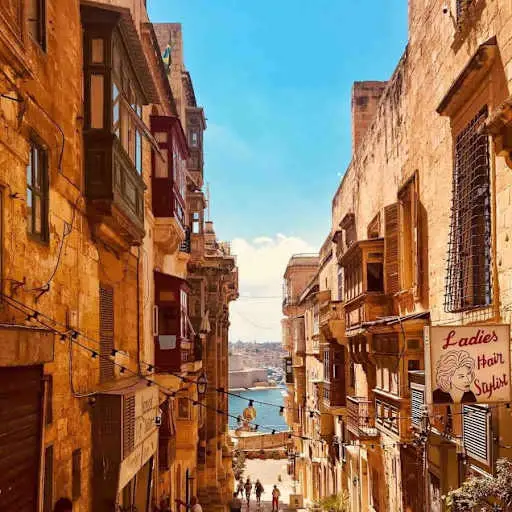 Narrow Valletta street in Malta lined with traditional enclosed balconies, sloping down to the harbor