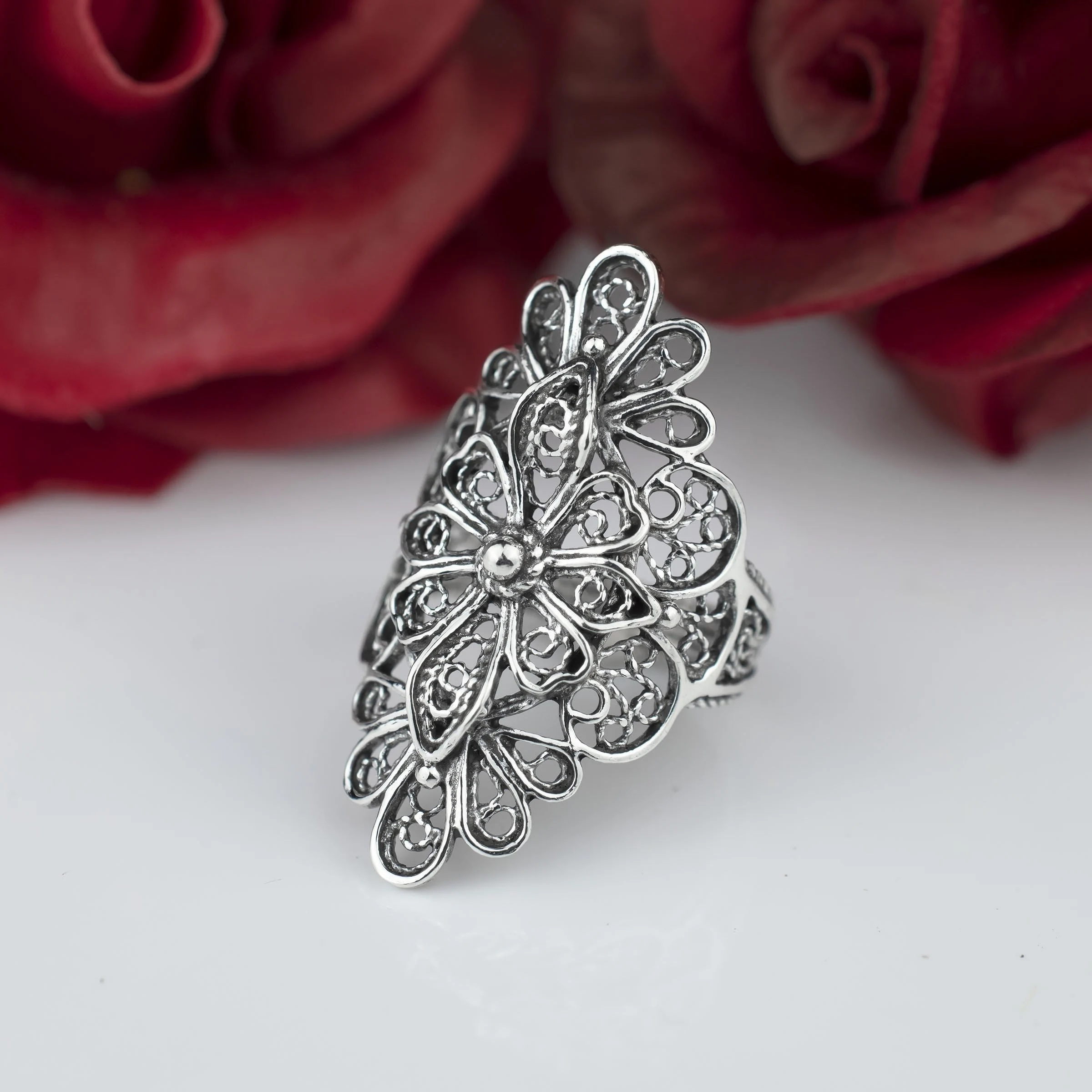 Maltese silver filigree ring with a floral design, displayed against red roses