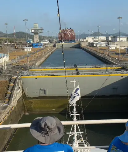 Cruise passengers at the rail watching a container ship ahead in a Panama Canal lock during a full transit