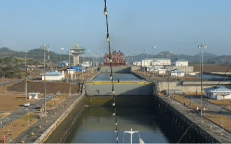 A container ship ahead in the Panama Canal locks with the control tower and green hills beyond.