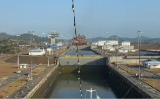 A container ship ahead in the Panama Canal locks with the control tower and green hills beyond.